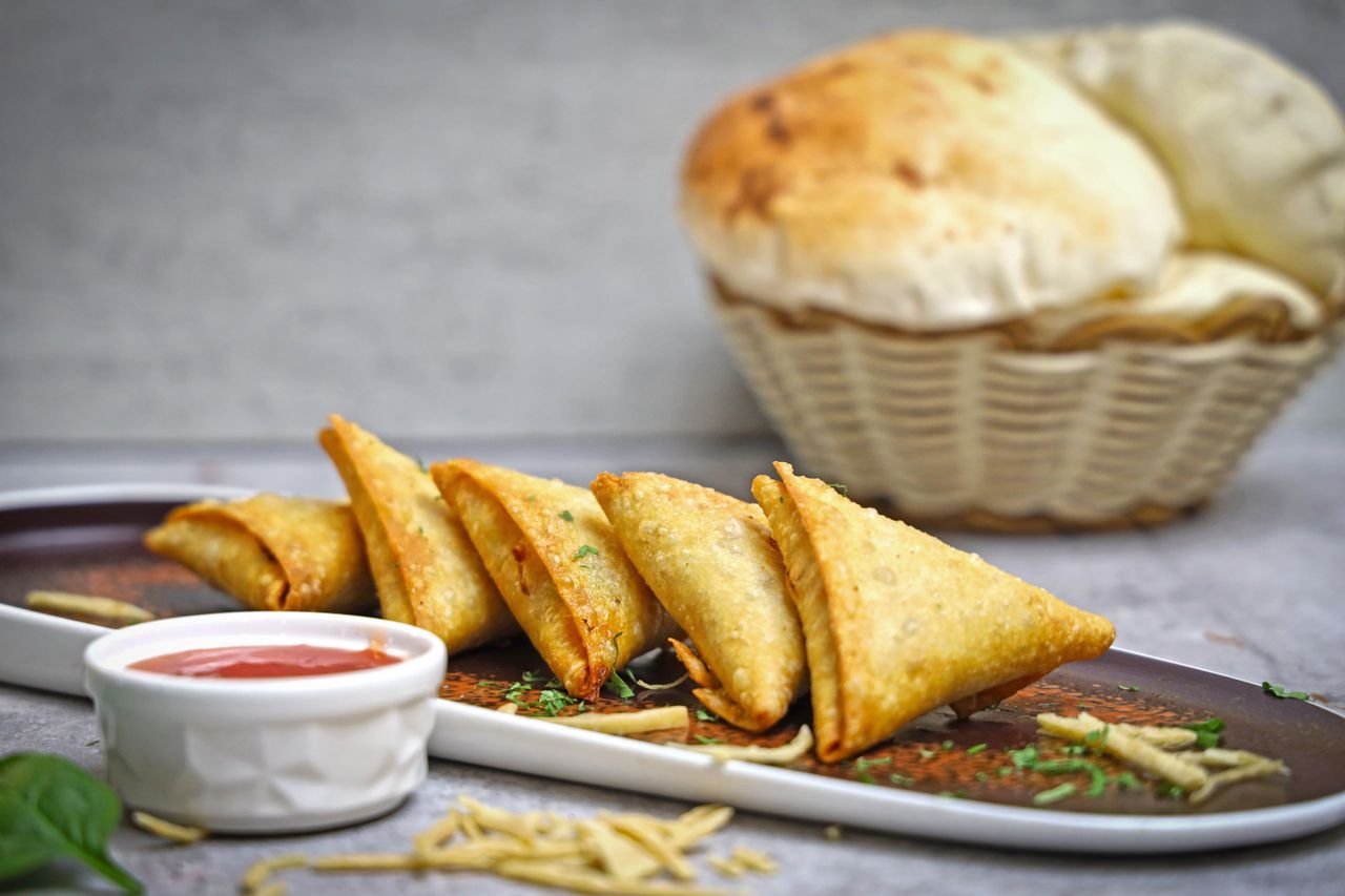 Golden fried samosas served with dipping sauce on a plate, perfect snack or appetizer.