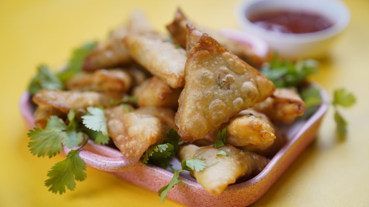 A plate of golden, crispy samosas garnished with cilantro, served with a side of dipping sauce.